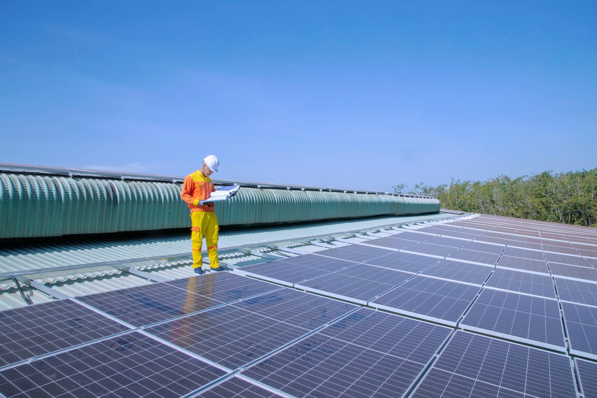 A solar technician inspects solar panels on a rooftop under a clear blue sky, promoting renewable energy.