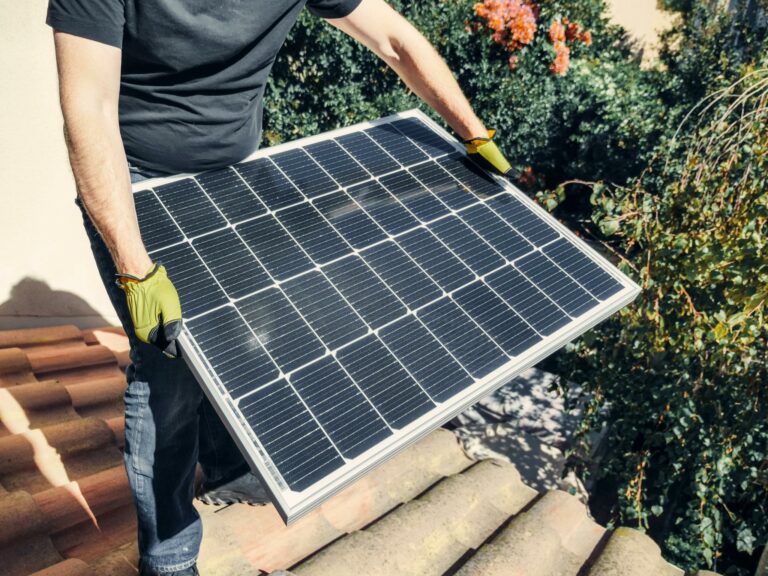 A worker in gloves installs a solar panel on a tiled rooftop, promoting renewable energy.